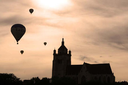 photographie de la basilique de Dole, au couché de soleil, avec des montgolfières en vol